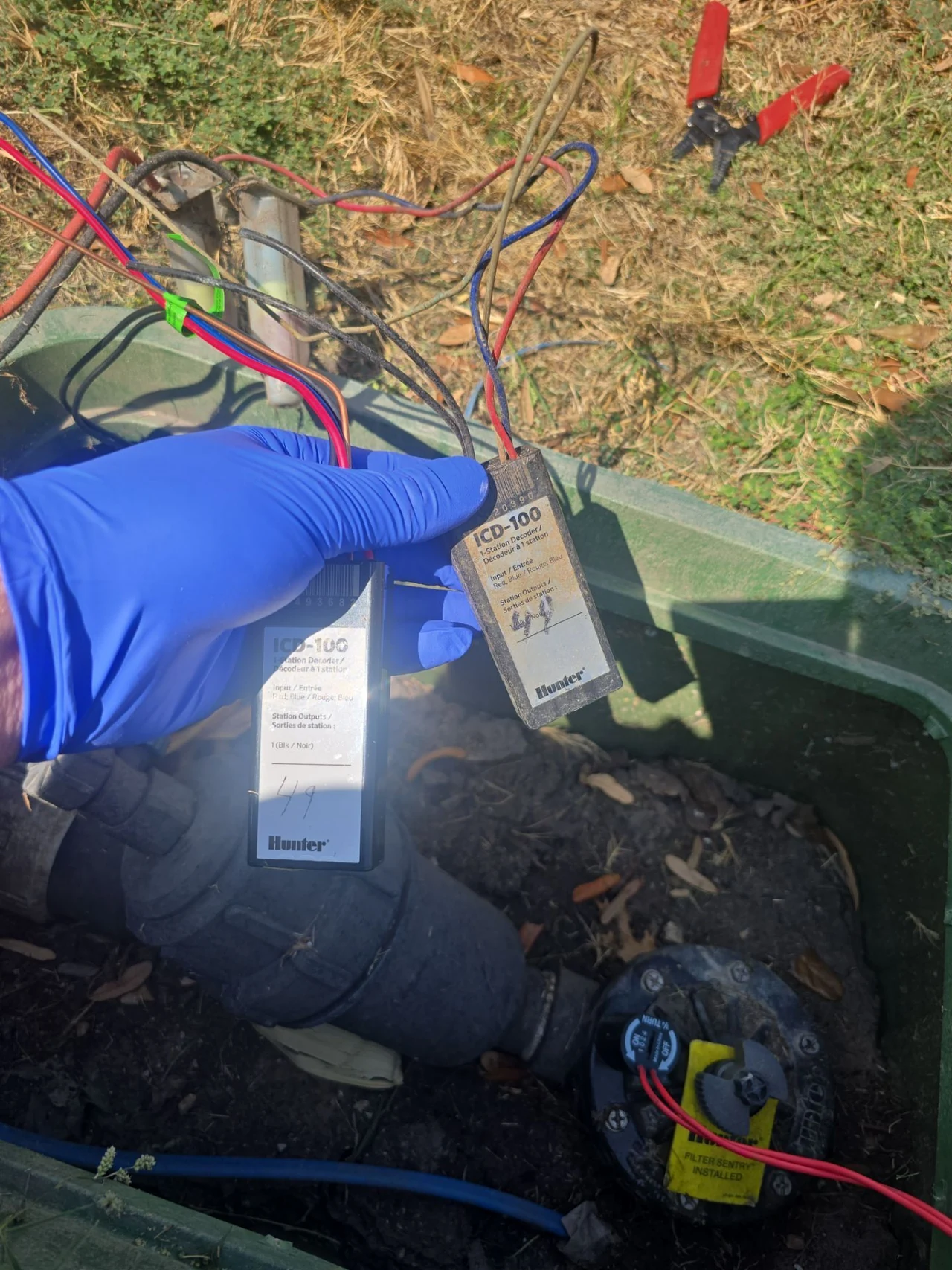 Blue-gloved hand holding two Hunter ICD-100 irrigation decoders in the field.