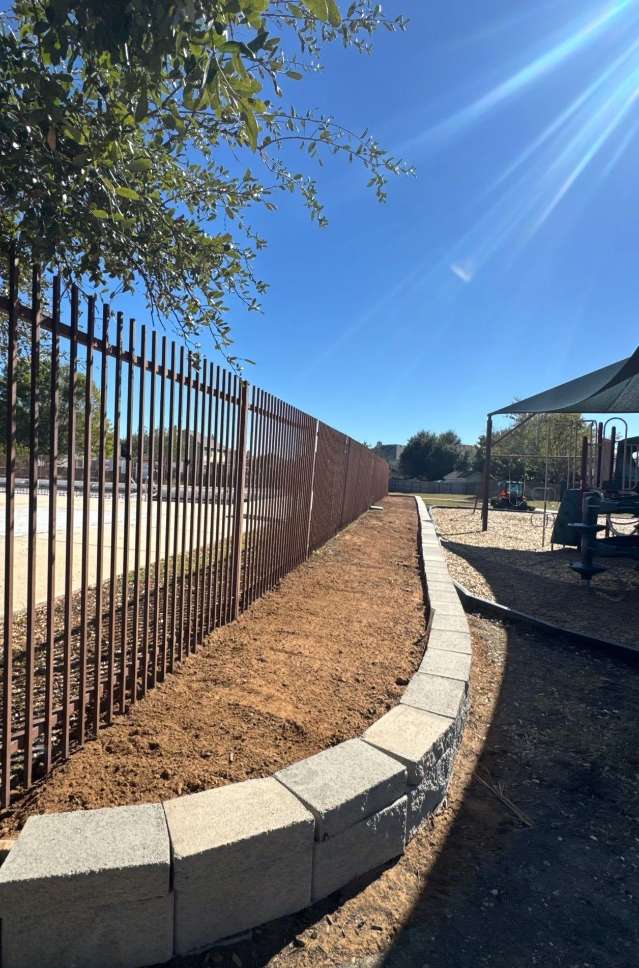 Curved retaining wall for a ground-cover planter separating a pool and playground.